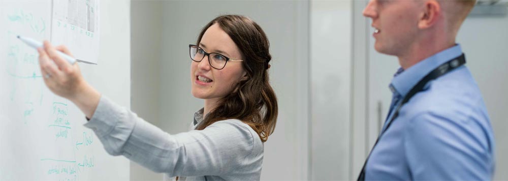 Image of a woman drawing on a white board discussing a development project to another man in a blue shirt