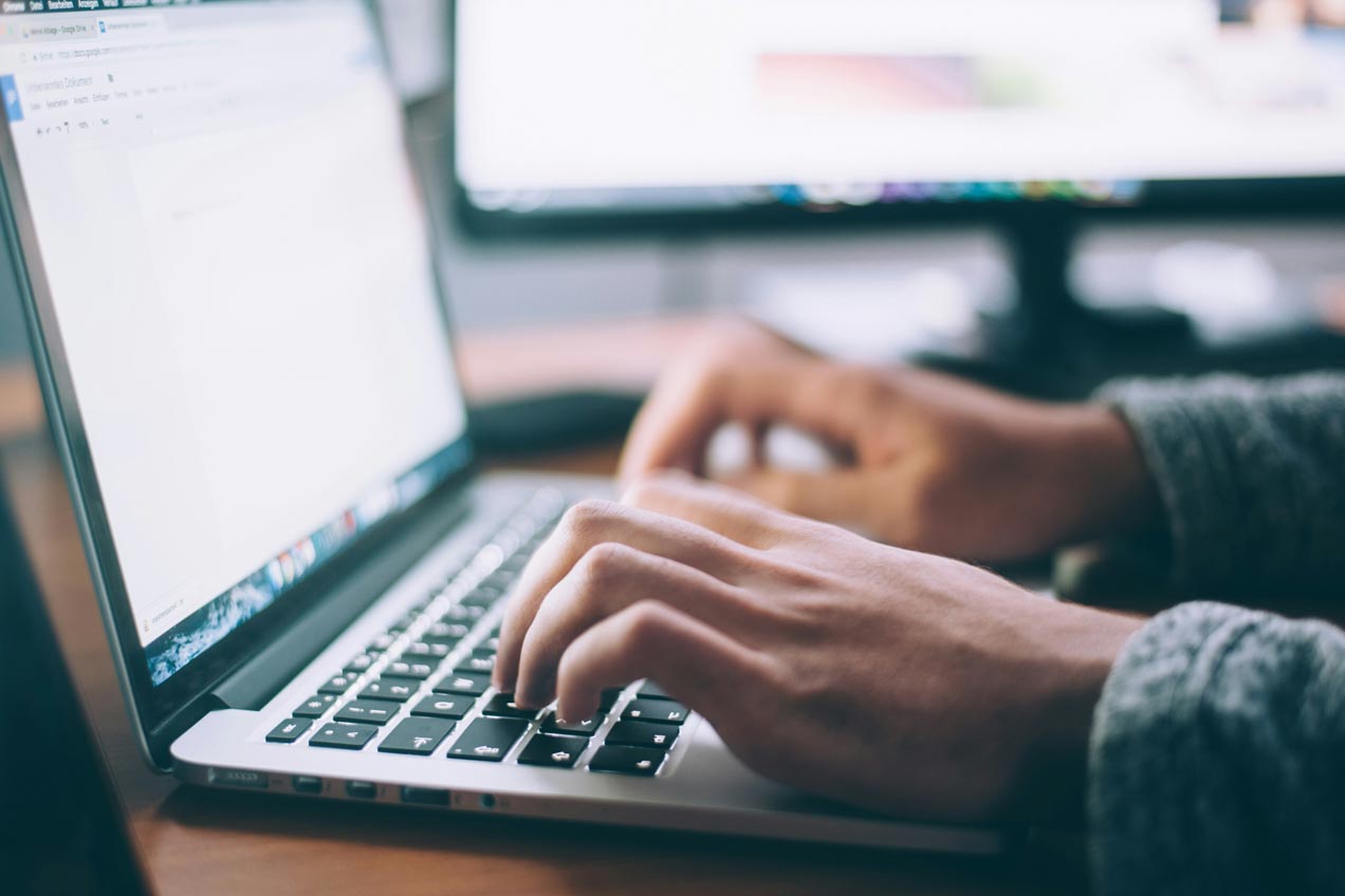 A close up of a software developer's hands typing on a laptop in an office environment.